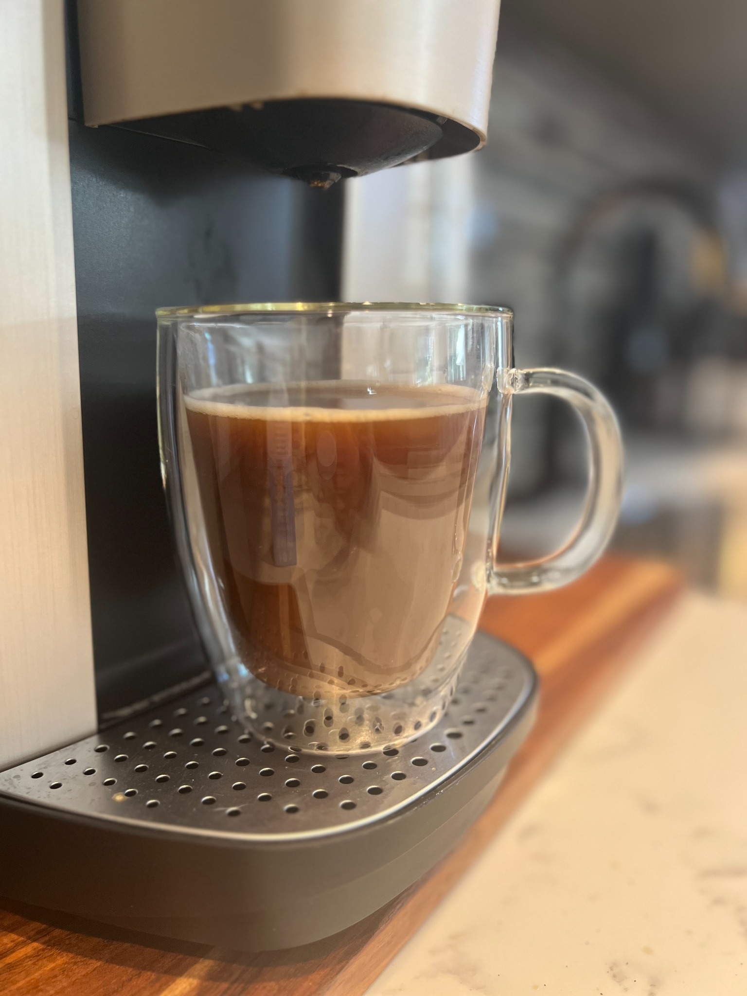 Double-wall glass coffee mug filled with coffee beneath an espresso machine