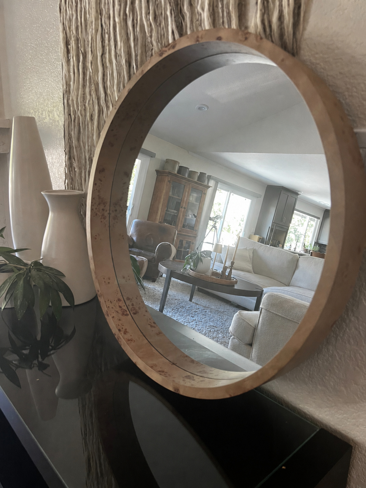 Round burlwood-grain mirror styled on a dark console in a warm neutral living room